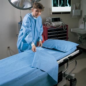 A woman in blue scrubs putting a sheet on a bed.