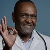 A black man in a lab coat making an ok gesture.